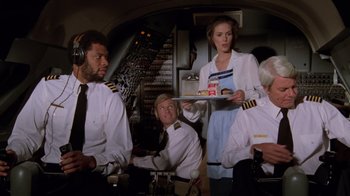 Movie still from “Airplane!” (1980), directed by David Zucker – A group of people standing in a room with a tray of food; Medium shot, Low angle