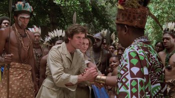 Movie still from “Airplane!” (1980), directed by David Zucker – A group of people gathered around a man shaking hands with another man; Medium shot, Over the shoulder angle