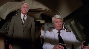 Movie still from “Airplane!” (1980), directed by David Zucker – Two men in suits and ties in a room; Medium shot, Low angle