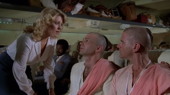 Movie still from “Airplane!” (1980), directed by David Zucker – A group of people sitting on top of an airplane next to each other; Medium shot, Low angle