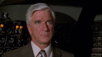 Movie still from “Airplane!” (1980), directed by David Zucker – An older man wearing a suit and tie; Close Up shot, High angle