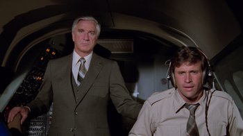 Movie still from “Airplane!” (1980), directed by David Zucker – A man and a man standing next to each other in an airplane; Medium shot, Low angle
