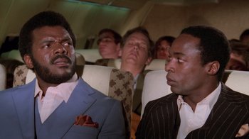 Movie still from “Airplane!” (1980), directed by David Zucker – A group of men sitting on a plane looking at each other; Close Up shot, Low angle