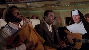 Movie still from “Airplane!” (1980), directed by David Zucker – A group of people sitting on a plane; Medium shot, High angle