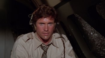 Movie still from “Airplane!” (1980), directed by David Zucker – A man wearing headphones and wearing a shirt and tie; Close Up shot, High angle