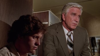 Movie still from “Airplane!” (1980), directed by David Zucker – Two men in suits and ties looking at each other; Close Up shot, Over the shoulder angle