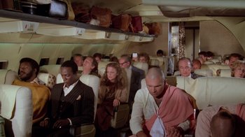 Movie still from “Airplane!” (1980), directed by David Zucker – A group of people sitting on a plane; Wide shot, High angle
