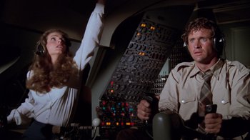 Movie still from “Airplane!” (1980), directed by David Zucker – A man and a woman are sitting next to each other in an airplane cockpit; Medium shot, Low angle