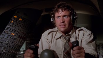 Movie still from “Airplane!” (1980), directed by David Zucker – A man wearing headphones and a tie holding a remote control; Close Up shot, Low angle