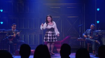 Movie still from “Alex Borstein: Corsets & Clown Suits” (2023), directed by Scott Ellis – A woman standing on a stage in front of an audience; Wide shot, Over the shoulder angle