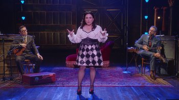 Movie still from “Alex Borstein: Corsets & Clown Suits” (2023), directed by Scott Ellis – A woman standing on a stage in front of an audience; Wide shot, Over the shoulder angle