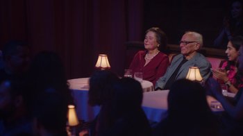 Movie still from “Alex Borstein: Corsets & Clown Suits” (2023), directed by Scott Ellis – A couple of people sitting at a dinner table; Wide shot, Over the shoulder angle