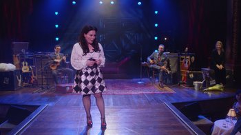 Movie still from “Alex Borstein: Corsets & Clown Suits” (2023), directed by Scott Ellis – A woman standing on a stage in front of a group of people; Wide shot, High angle