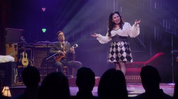 Movie still from “Alex Borstein: Corsets & Clown Suits” (2023), directed by Scott Ellis – A man and a woman on a stage singing; Wide shot, Over the shoulder angle