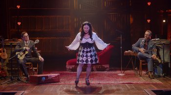 Movie still from “Alex Borstein: Corsets & Clown Suits” (2023), directed by Scott Ellis – A woman standing on a stage in front of a microphone; Wide shot, Over the shoulder angle