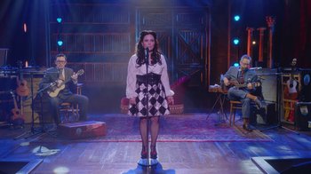 Movie still from “Alex Borstein: Corsets & Clown Suits” (2023), directed by Scott Ellis – A woman standing on a stage holding a microphone; Wide shot, Over the shoulder angle