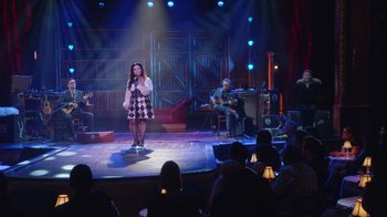 Movie still from “Alex Borstein: Corsets & Clown Suits” (2023), directed by Scott Ellis – A woman standing on a stage singing into a microphone; Extreme Wide shot, High angle