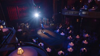 Movie still from “Alex Borstein: Corsets & Clown Suits” (2023), directed by Scott Ellis – A man standing on a stage in front of an audience; Extreme Wide shot, High angle