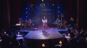 Movie still from “Alex Borstein: Corsets & Clown Suits” (2023), directed by Scott Ellis – A woman standing on a stage in front of a group of people; Extreme Wide shot, Over the shoulder angle