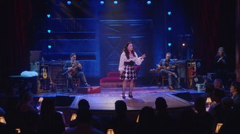 Movie still from “Alex Borstein: Corsets & Clown Suits” (2023), directed by Scott Ellis – A woman standing on a stage with a microphone; Wide shot, Over the shoulder angle