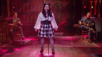 Movie still from “Alex Borstein: Corsets & Clown Suits” (2023), directed by Scott Ellis – A woman standing on a stage singing into a microphone; Wide shot, High angle