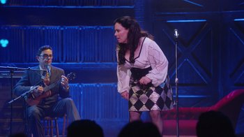 Movie still from “Alex Borstein: Corsets & Clown Suits” (2023), directed by Scott Ellis – A woman standing on a stage next to a microphone; Wide shot, Over the shoulder angle