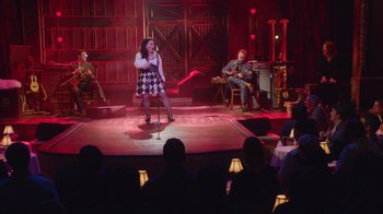 Movie still from “Alex Borstein: Corsets & Clown Suits” (2023), directed by Scott Ellis – A woman singing on a stage while a man plays the guitar; Wide shot, High angle