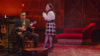Movie still from “Alex Borstein: Corsets & Clown Suits” (2023), directed by Scott Ellis – A woman standing on a stage with a guitar; Wide shot, High angle
