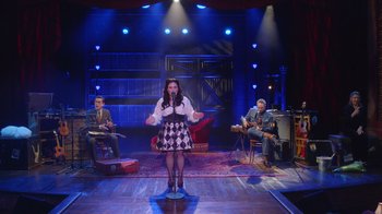 Movie still from “Alex Borstein: Corsets & Clown Suits” (2023), directed by Scott Ellis – A group of people sitting on a stage with a microphone; Wide shot, High angle