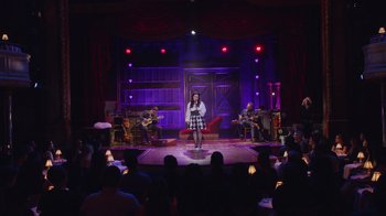 Movie still from “Alex Borstein: Corsets & Clown Suits” (2023), directed by Scott Ellis – A woman standing on a stage in front of a group of people; Extreme Wide shot, Over the shoulder angle