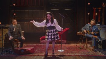 Movie still from “Alex Borstein: Corsets & Clown Suits” (2023), directed by Scott Ellis – A woman standing on a stage in front of a microphone; Wide shot, High angle