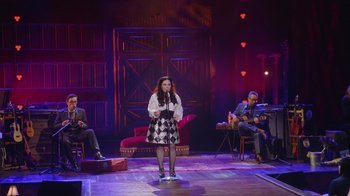 Movie still from “Alex Borstein: Corsets & Clown Suits” (2023), directed by Scott Ellis – A woman standing on a stage holding a microphone; Wide shot, High angle