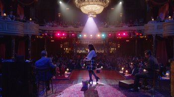 Movie still from “Alex Borstein: Corsets & Clown Suits” (2023), directed by Scott Ellis – A woman standing on a stage in front of an audience; Extreme Wide shot, Over the shoulder angle
