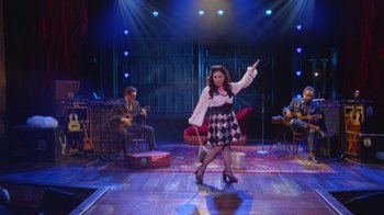Movie still from “Alex Borstein: Corsets & Clown Suits” (2023), directed by Scott Ellis – A woman in a checkered dress on a stage; Wide shot, High angle
