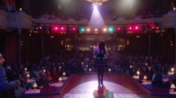 Movie still from “Alex Borstein: Corsets & Clown Suits” (2023), directed by Scott Ellis – A woman standing on a stage in front of an audience; Extreme Wide shot, High angle