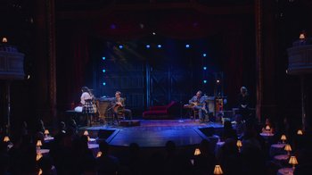 Movie still from “Alex Borstein: Corsets & Clown Suits” (2023), directed by Scott Ellis – A group of people sitting on a stage playing musical instruments; Extreme Wide shot, High angle