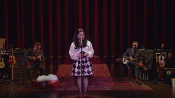 Movie still from “Alex Borstein: Corsets & Clown Suits” (2023), directed by Scott Ellis – A woman standing on a stage holding a microphone; Wide shot, High angle