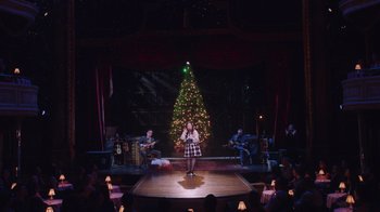 Movie still from “Alex Borstein: Corsets & Clown Suits” (2023), directed by Scott Ellis – A woman singing in front of a christmas tree; Extreme Wide shot, High angle