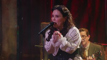 Movie still from “Alex Borstein: Corsets & Clown Suits” (2023), directed by Scott Ellis – A woman is singing into a microphone on a stage; Close Up shot, Over the shoulder angle