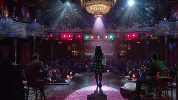 Movie still from “Alex Borstein: Corsets & Clown Suits” (2023), directed by Scott Ellis – A woman standing in front of an audience on a stage; Extreme Wide shot, High angle
