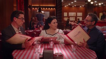 Movie still from “Alex Borstein: Corsets & Clown Suits” (2023), directed by Scott Ellis – A woman sitting at a table in front of two other women; Medium shot, Over the shoulder angle
