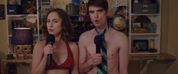Movie still from “Alex Strangelove” (2018), directed by Craig Johnson – A man and a woman holding microphones in a room; Medium shot, Over the shoulder angle