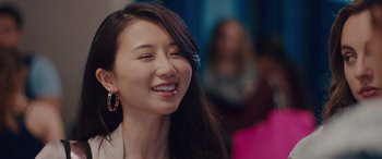 Movie still from “Alex Strangelove” (2018), directed by Craig Johnson – A woman with long black hair smiles at the camera; Close Up shot, Over the shoulder angle