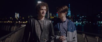 Movie still from “Alex Strangelove” (2018), directed by Craig Johnson – Two young men standing next to each other on a city street at night; Medium shot, Over the shoulder angle