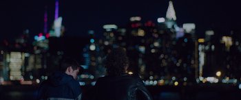 Movie still from “Alex Strangelove” (2018), directed by Craig Johnson – Two people standing in front of a city skyline at night; Wide shot, Over the shoulder angle