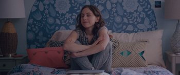 Movie still from “Alex Strangelove” (2018), directed by Craig Johnson – A girl sitting on a bed with her arms crossed; Medium shot, High angle