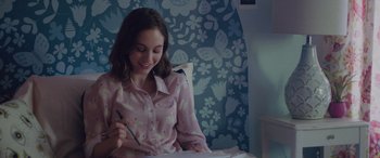 Movie still from “Alex Strangelove” (2018), directed by Craig Johnson – A young girl sitting at a table writing on a piece of paper; Medium shot, Over the shoulder angle