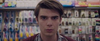 Movie still from “Alex Strangelove” (2018), directed by Craig Johnson – A young man with brown hair wearing a plaid shirt; Close Up shot, Over the shoulder angle