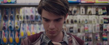 Movie still from “Alex Strangelove” (2018), directed by Craig Johnson – A man looking at his cell phone while standing in a store; Close Up shot, Over the shoulder angle