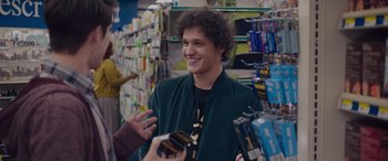Movie still from “Alex Strangelove” (2018), directed by Craig Johnson – A young man smiles while talking to a woman in a store; Close Up shot, Over the shoulder angle